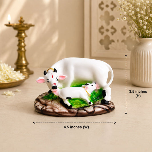 A white cow and calf figurine with green accents on a brown textured base, shown on a beige surface with decorative props in the background and measurement arrows indicating 4.5 inches wide by 3.