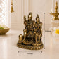 A small bronze-colored Hindu deity statue shown on a light surface with overlaid dimension arrows and text reading 6 inches tall and 5 inches wide. The background is softly blurred with decorative objects and warm indoor lighting.